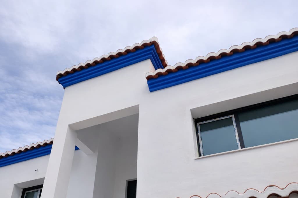 Fachada con pintura blanca y remate azul bajo tejas