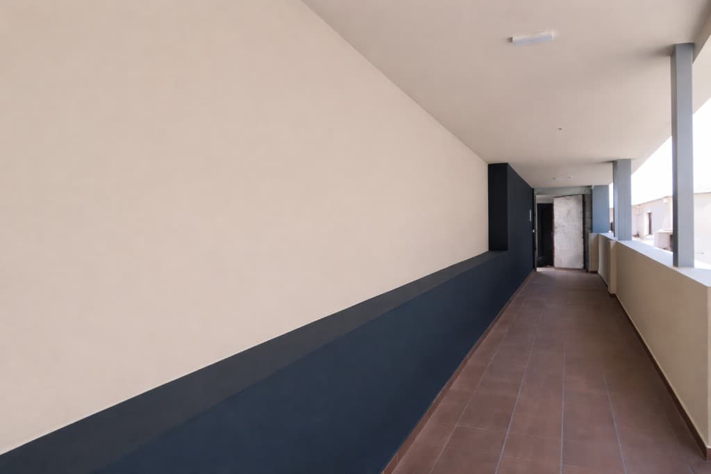 Pasillo exterior pintado, pared beige y zócalo azul